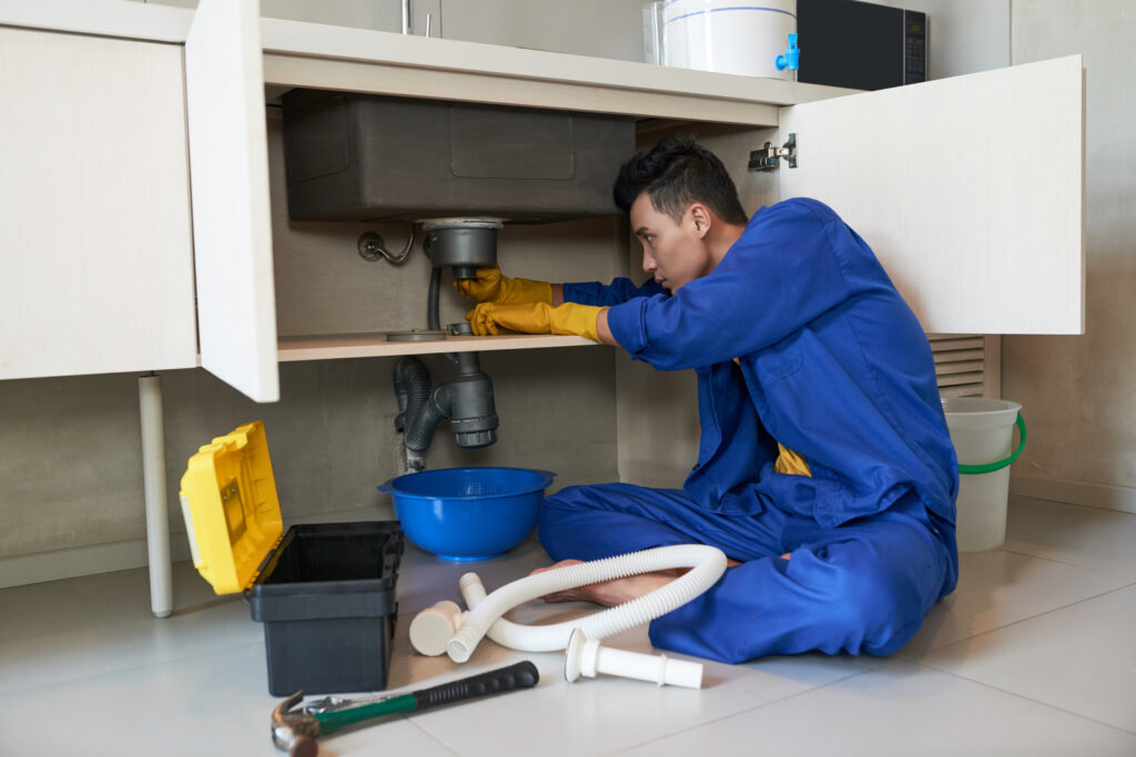 A technician fixing a kitchen drain during emergency sewage cleanup.