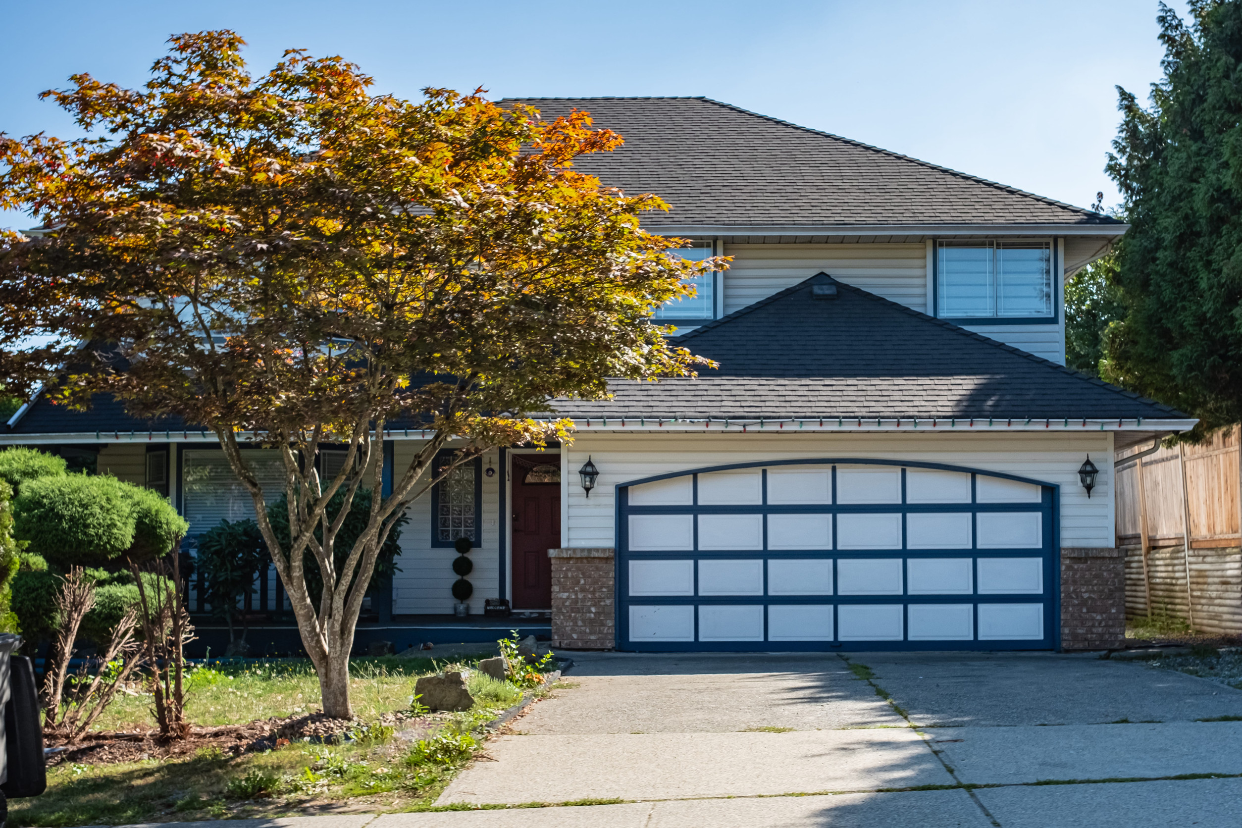 A well-maintained two-story suburban home with an attached front-facing garage, wide driveway, landscaped yard, and mature trees in a quiet residential neighborhood.
